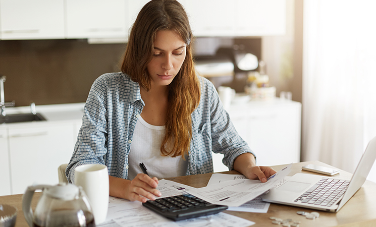 Mujer revisando papeles y utilizando calculadora
